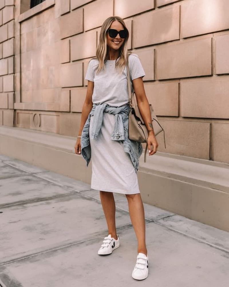 jaqueta jeans na cintura para look com tênis branco e vestido midi 